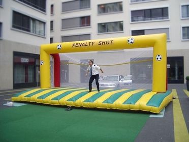 Auf einem Fußballfeld stehen mehrere transparente Bubble-Soccer-Anzüge in Blau und Rot einander gegenüber. Ein weißer Ball liegt in der Mitte. Im Hintergrund sind Fußballtore und Bäume zu sehen.