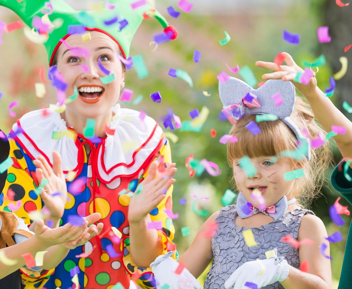Ein fröhlicher Clown und ein verkleidetes Kind feiern mit buntem Konfetti.